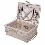 A beige picnic basket containing plates, cutlery, glasses, and salt and pepper pots, with a wicker base and a leather strap.