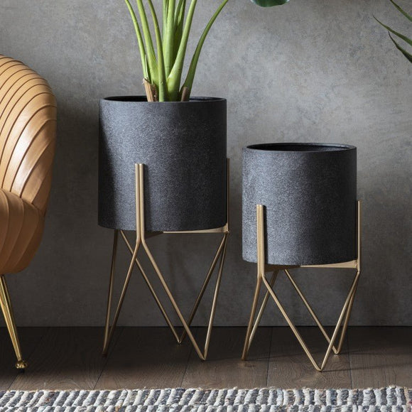 Two modern KHEE plant pots in a dark grey speckled finish, set on elegant gold geometric metal stands, showcasing stylish home decor and interior styling.