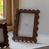 Wooden photo frame with scalloped edge on a surface near a window.