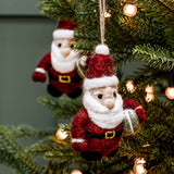 Handmade felted wool Santa Claus ornaments hanging on a decorated Christmas tree with warm string lights.