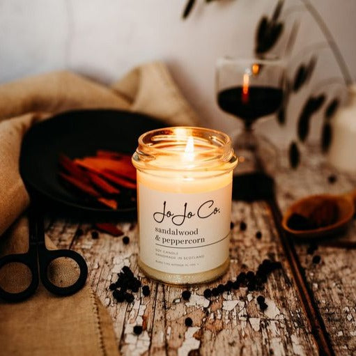 a sandalwood and peppercorn scented candle, lit on a wooden surface