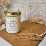 Candle jar with gold lid and 'Teacher Thank You Very Much' label on a textured surface.