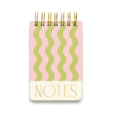 A spiral-bound notebook with a pink cover featuring vertical wavy stripes in light green and a cream-colored bottom section with the word 'NOTES' in gold lettering.