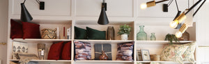 KHEE homeware display shelves featuring various decor items including red velvet cushions, green throw pillows, decorative glass vases, woven baskets, candles, and modern lighting fixtures.